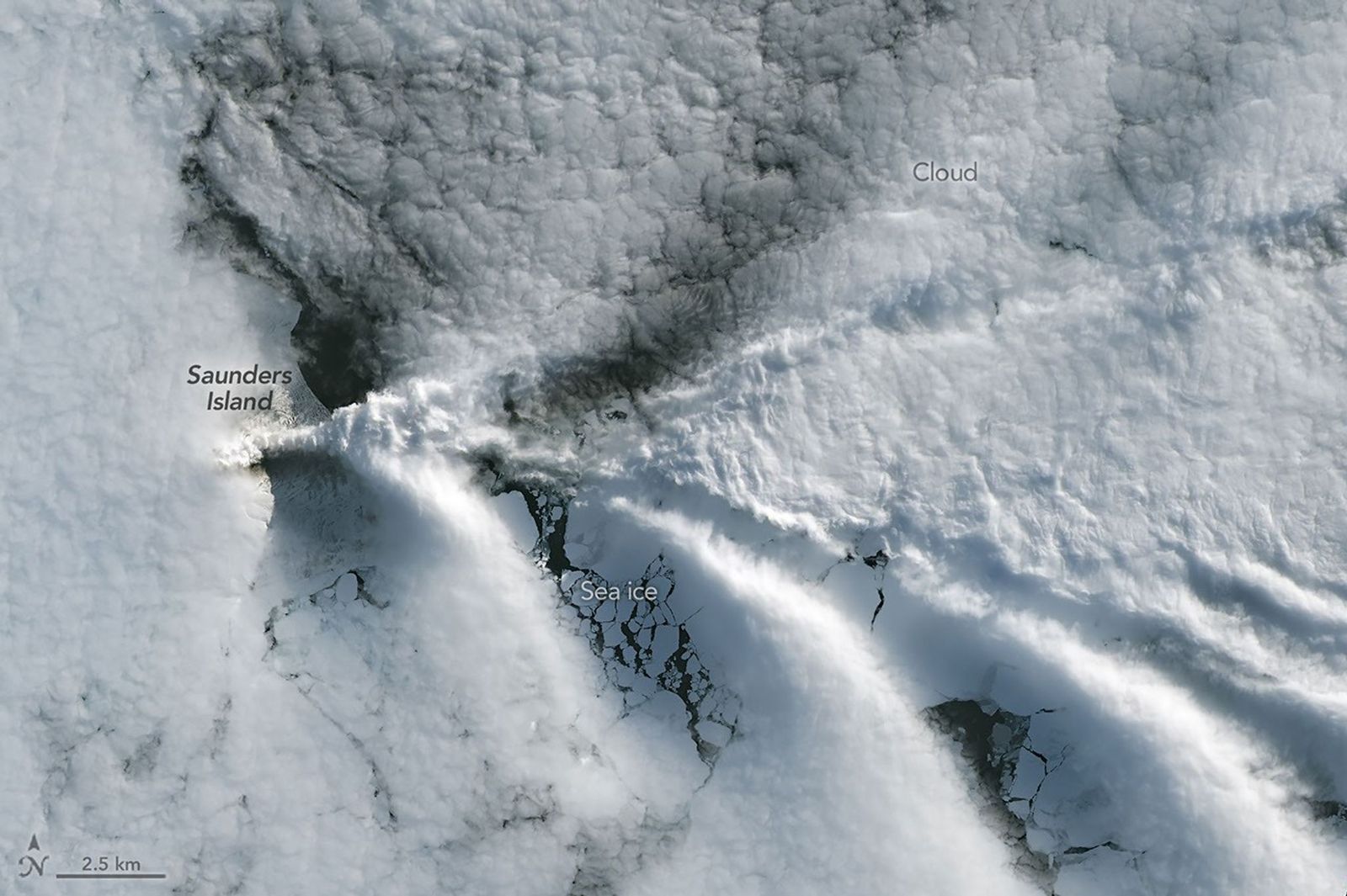 A series of V-shaped wave clouds appears over an ocean filled with pieces of sea ice.