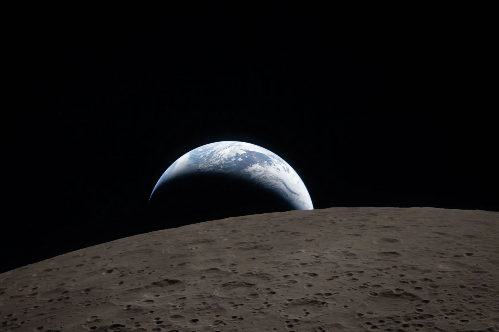 art002e009288 (April 6, 2026) – Earthset captured through the Orion spacecraft window at 6:41 p.m. EDT, April 6, 2026, during the Artemis II crew’s flyby of the Moon. A muted blue Earth with bright white clouds sets behind the cratered lunar surface. The dark portion of Earth is experiencing nighttime. On Earth’s day side, swirling clouds are visible over the Australia and Oceania region. In the foreground, Ohm crater has terraced edges and a flat floor interrupted by central peaks. Central peak