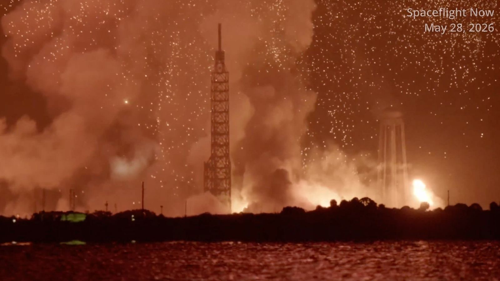 long-distance photo of a fireball and large smoke cloud over a launch pad at night
