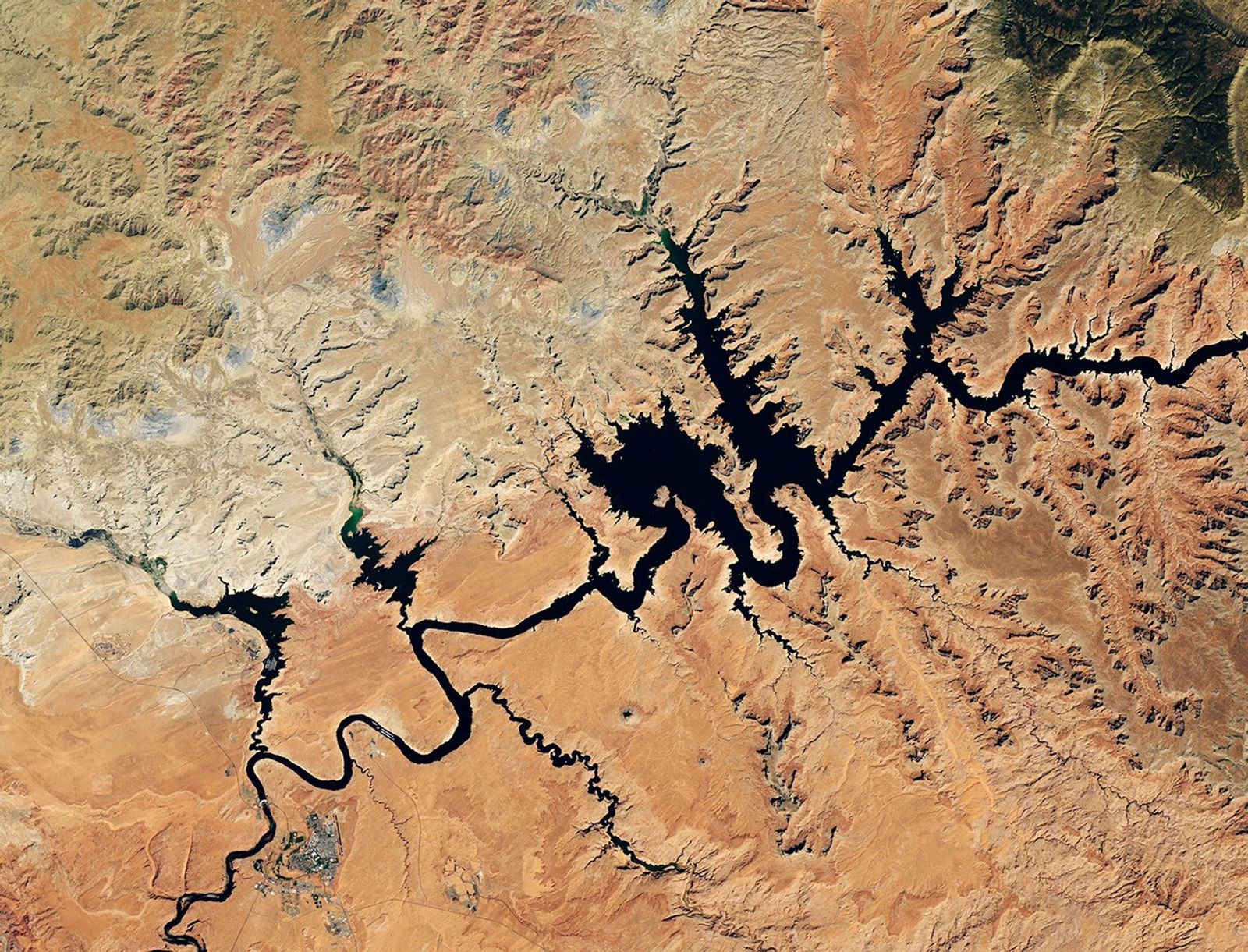 Water in Lake Powell is at record-low levels and looks like a wide river winding through a light orange desert landscape. The Glen Canyon Dam and the town of Page, Arizona, are visible in the lower left.