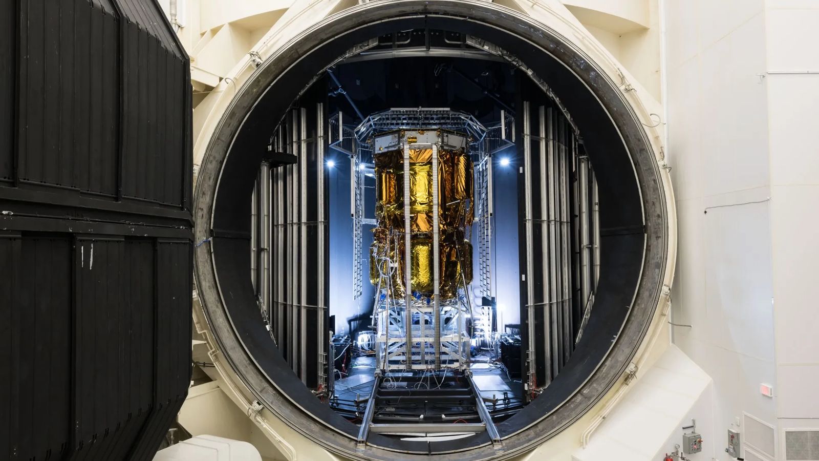 a gold-foiled spacecraft stands in a chamber with an open hatch