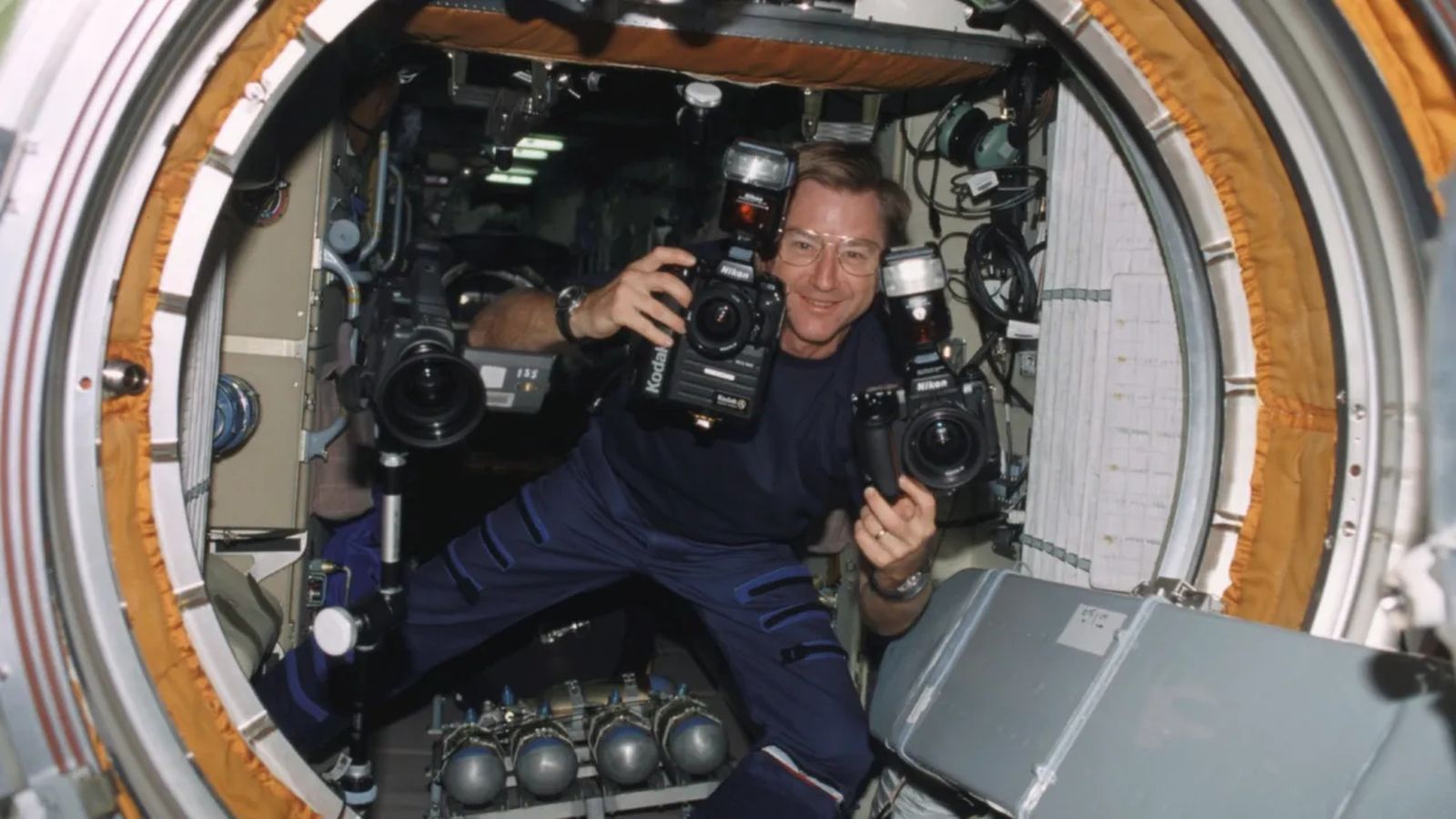 a man floats in zero gravity holding a camera in each hand