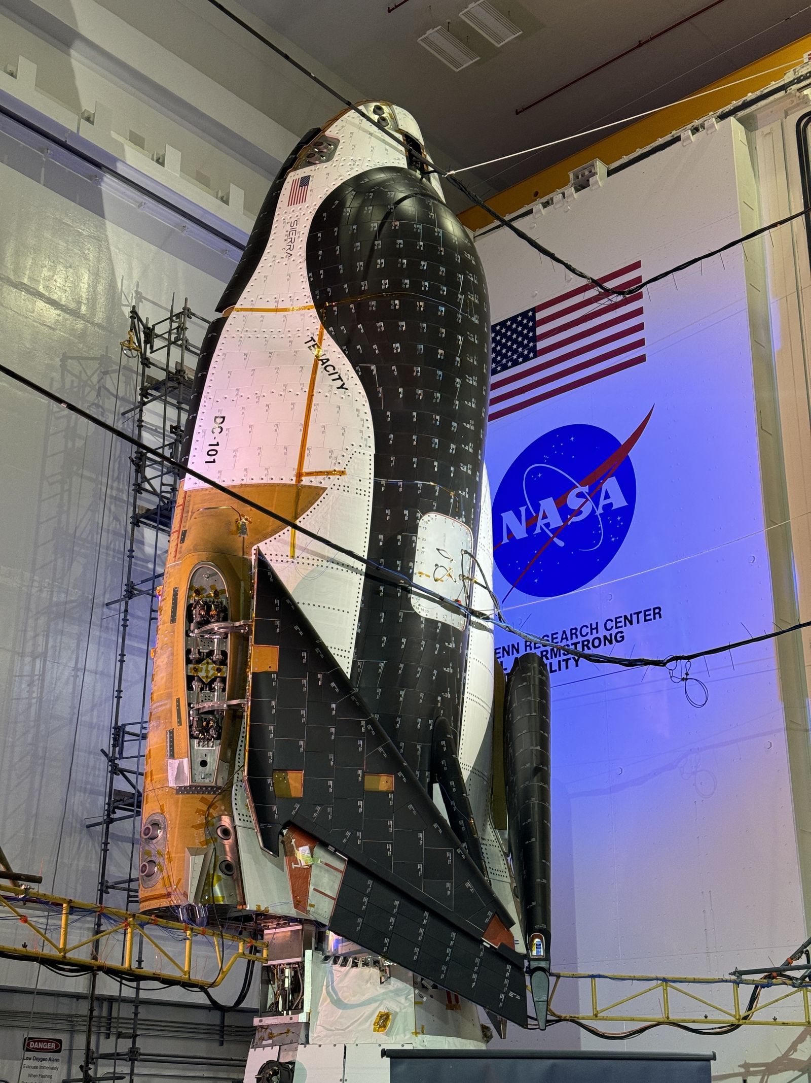 a black and white space plane stands on end in folded up in a hanger.