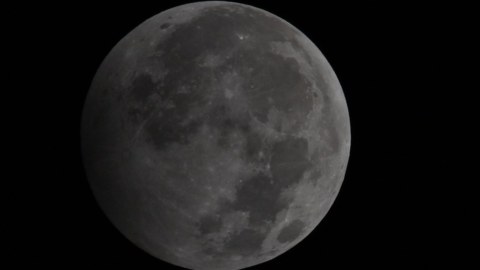A photograph showing the penumbral stage of a lunar eclipse as the lunar disk shines in a black night's sky.