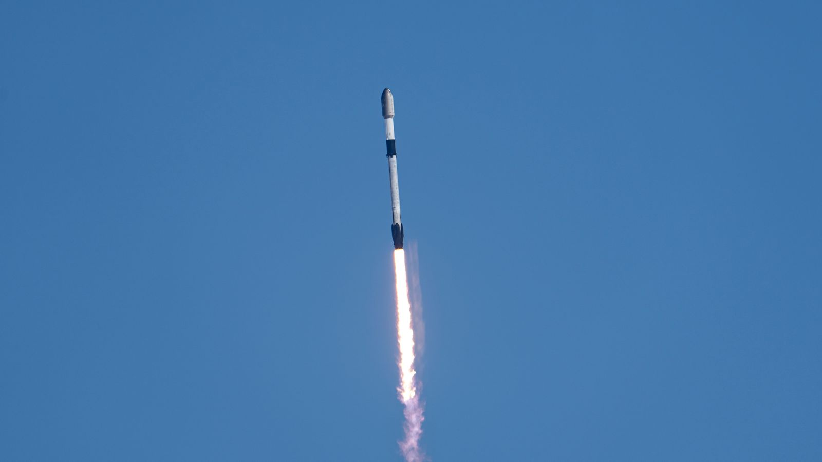 a black-and-white spacex falcon 9 rocket launches into a blue sky.