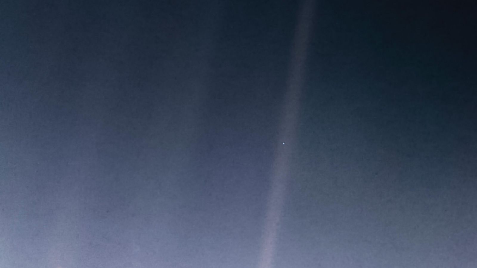 A hazy blueish image has one beam of light in the center-right. There's a tiny blue dot in the beam.