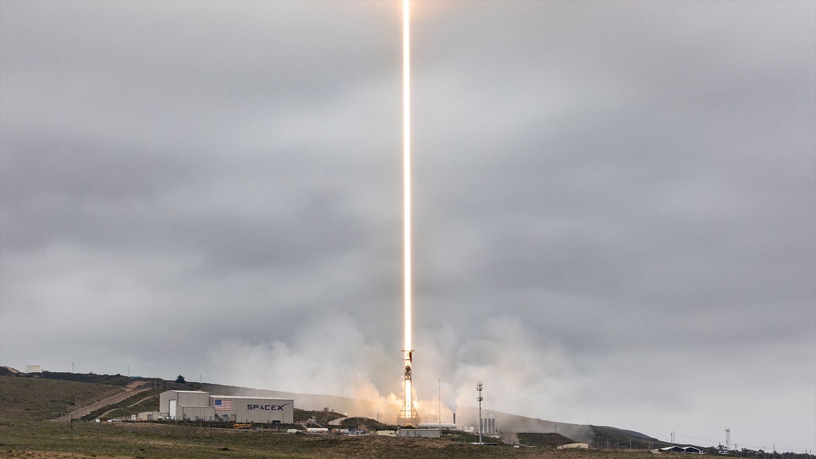 a timelapse exposure of a daytime rocket launch results in a bright beam of light climbing into the overcast sky