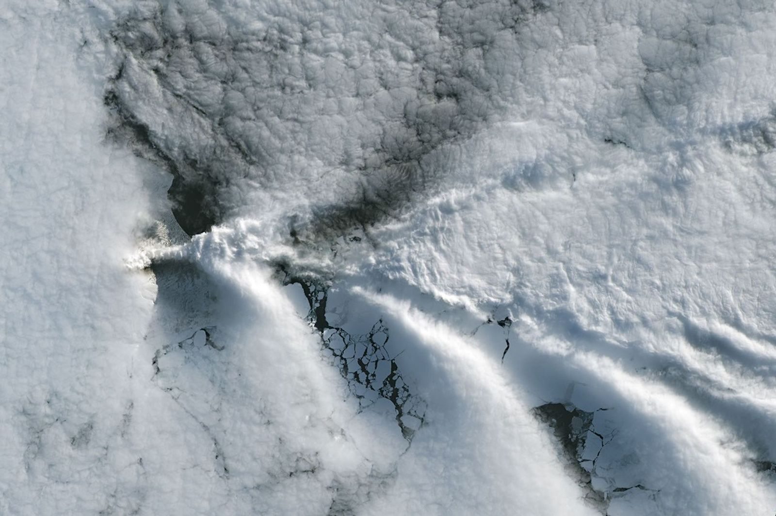 A series of V-shaped wave clouds appears over an ocean filled with pieces of sea ice.