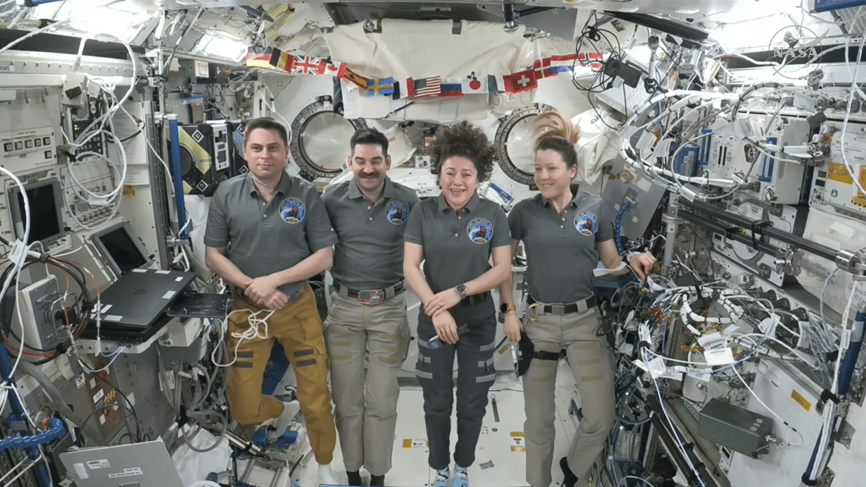 four people float in a space station module.