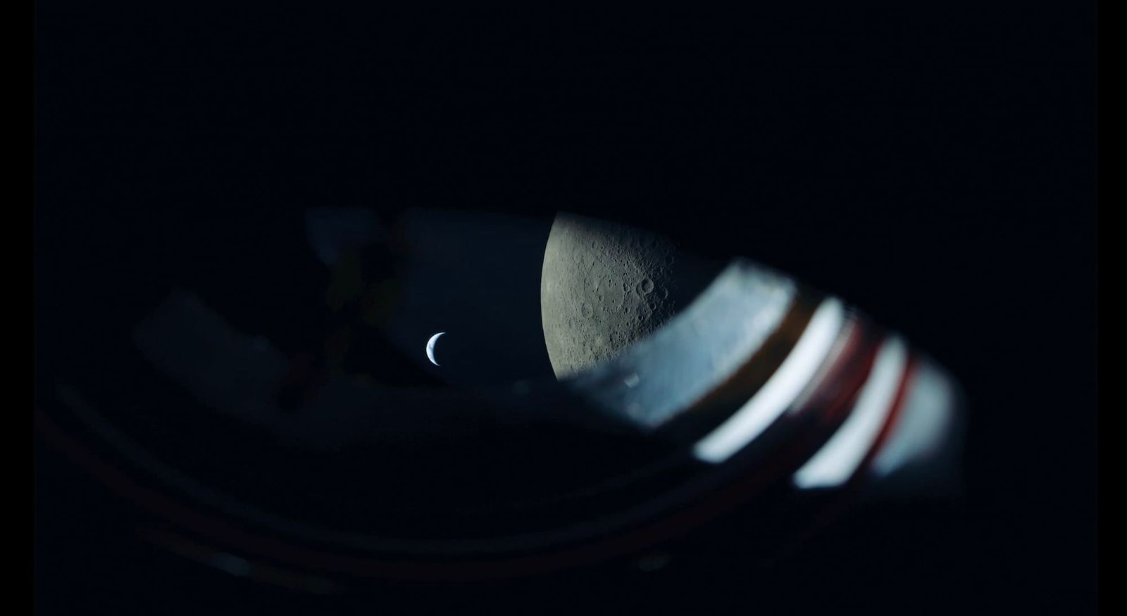 a view from the Artemis II spacecraft showing the edge of the window, the moon, and the earth as a tiny sliver