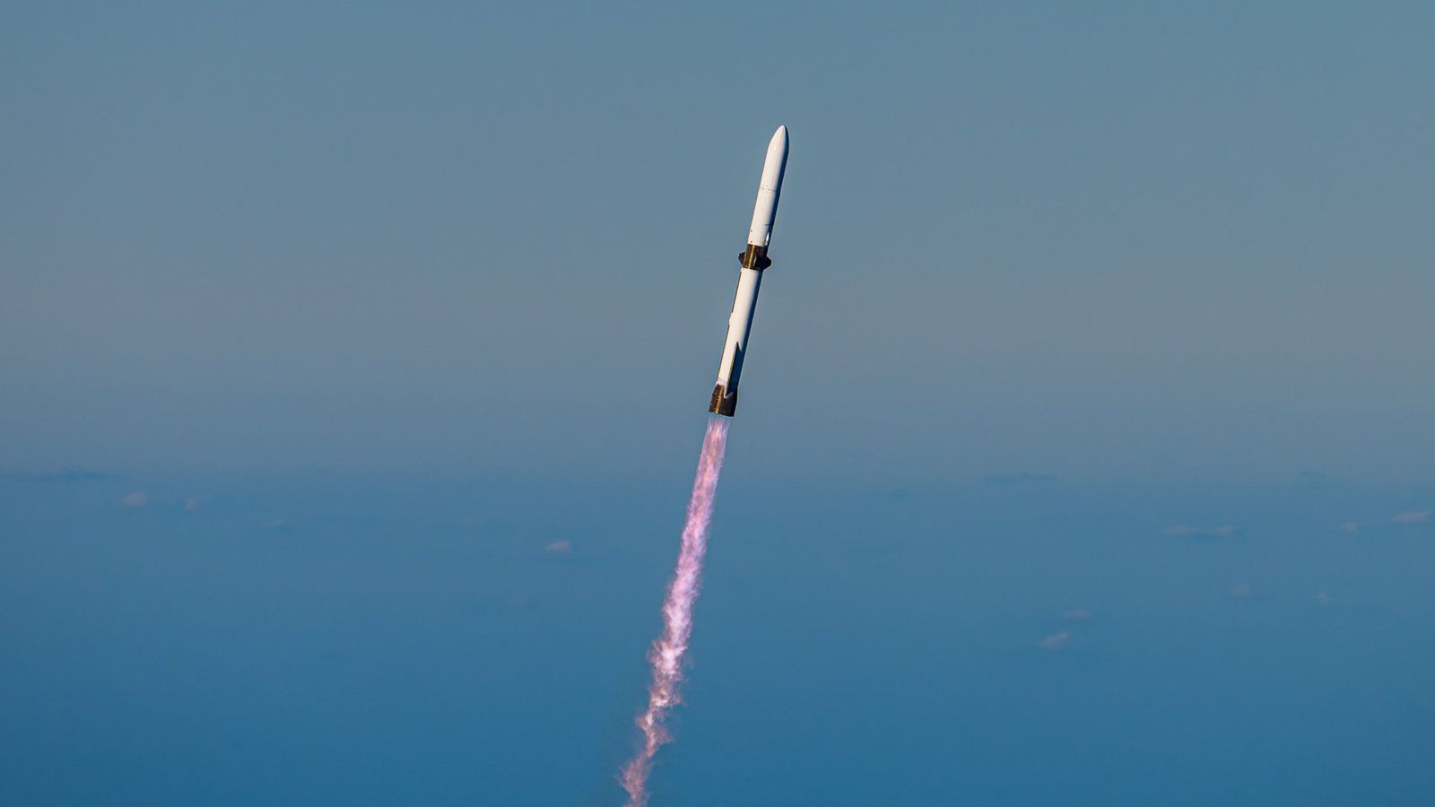 a white rocket climbs into a clear blue sky