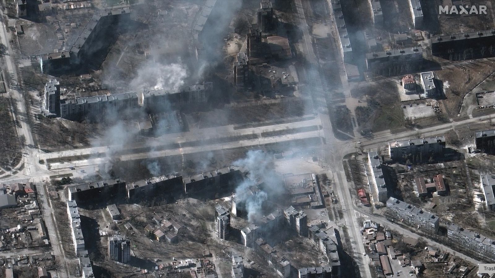 satellite photo of smoke rising from buildings in a neighborhood that has been destroyed by bombing