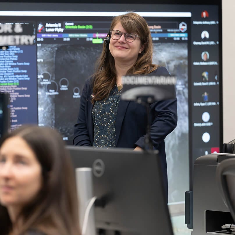 Marie Henderson, standing, and fellow members of the Artemis lunar science team listen as the Artemis II crew shares observations during the lunar flyby