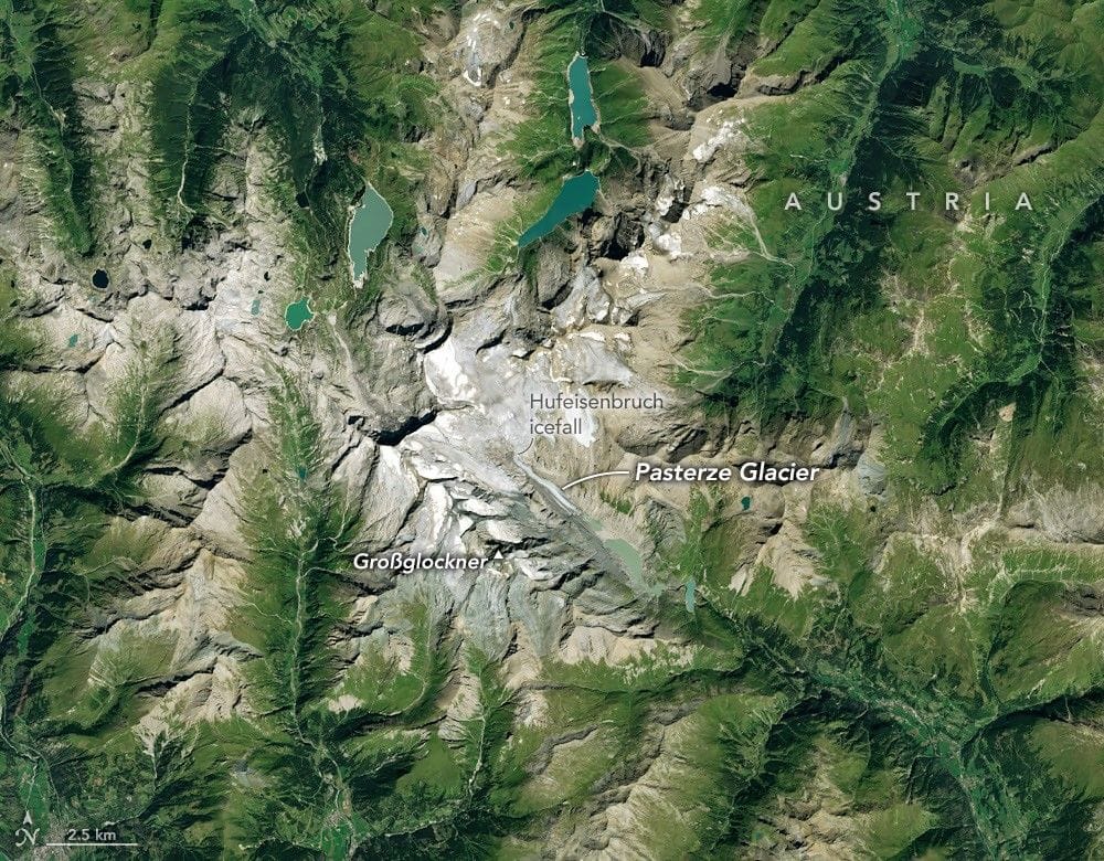 Ice in a broad Alpine basin connects with a short, narrow stretch of glacial ice in the valley below through one small icefall. Lakes fill much of the valley beyond the glacier’s terminus.