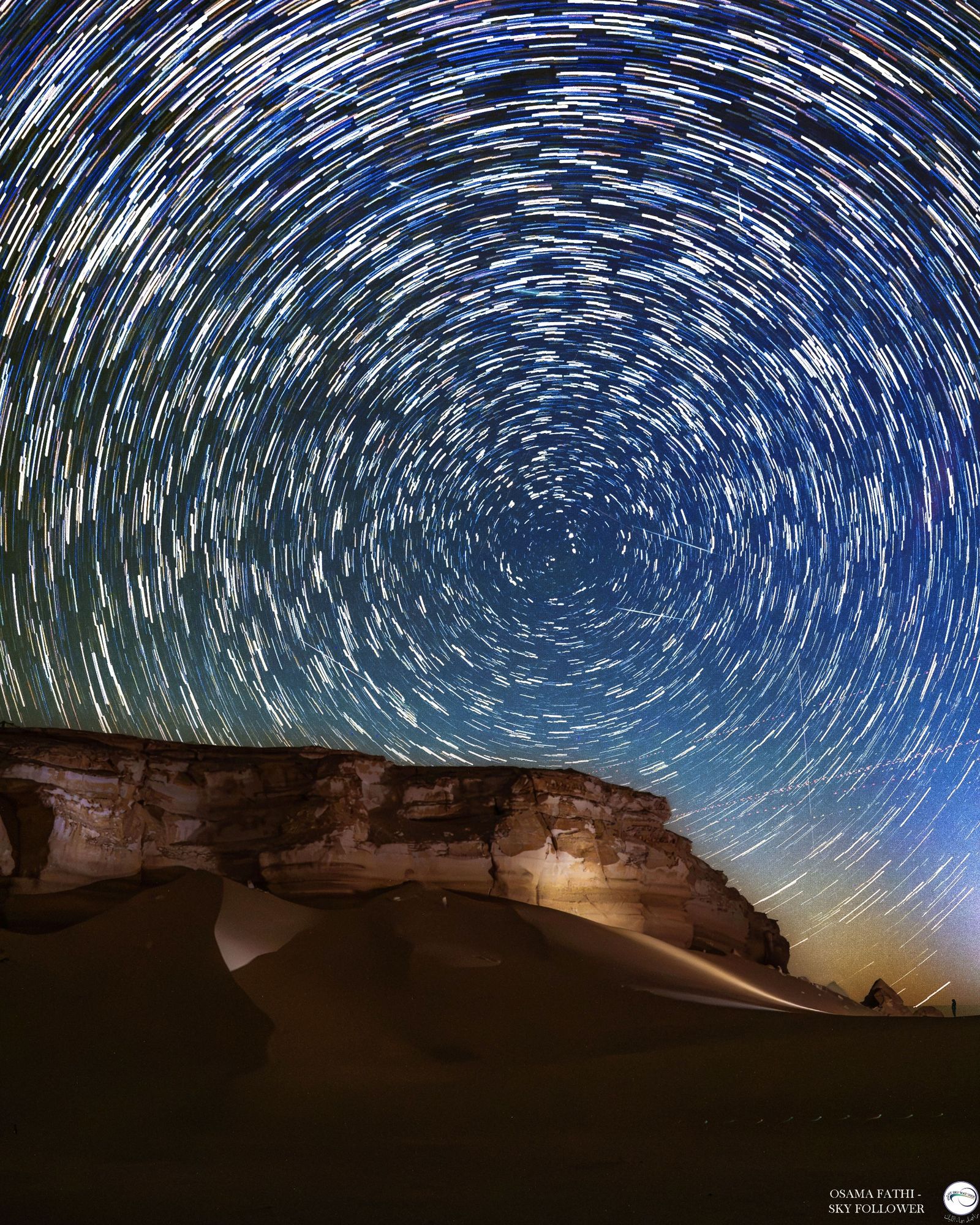 Star trails circle above a desert at night as meteors streak through the sky.