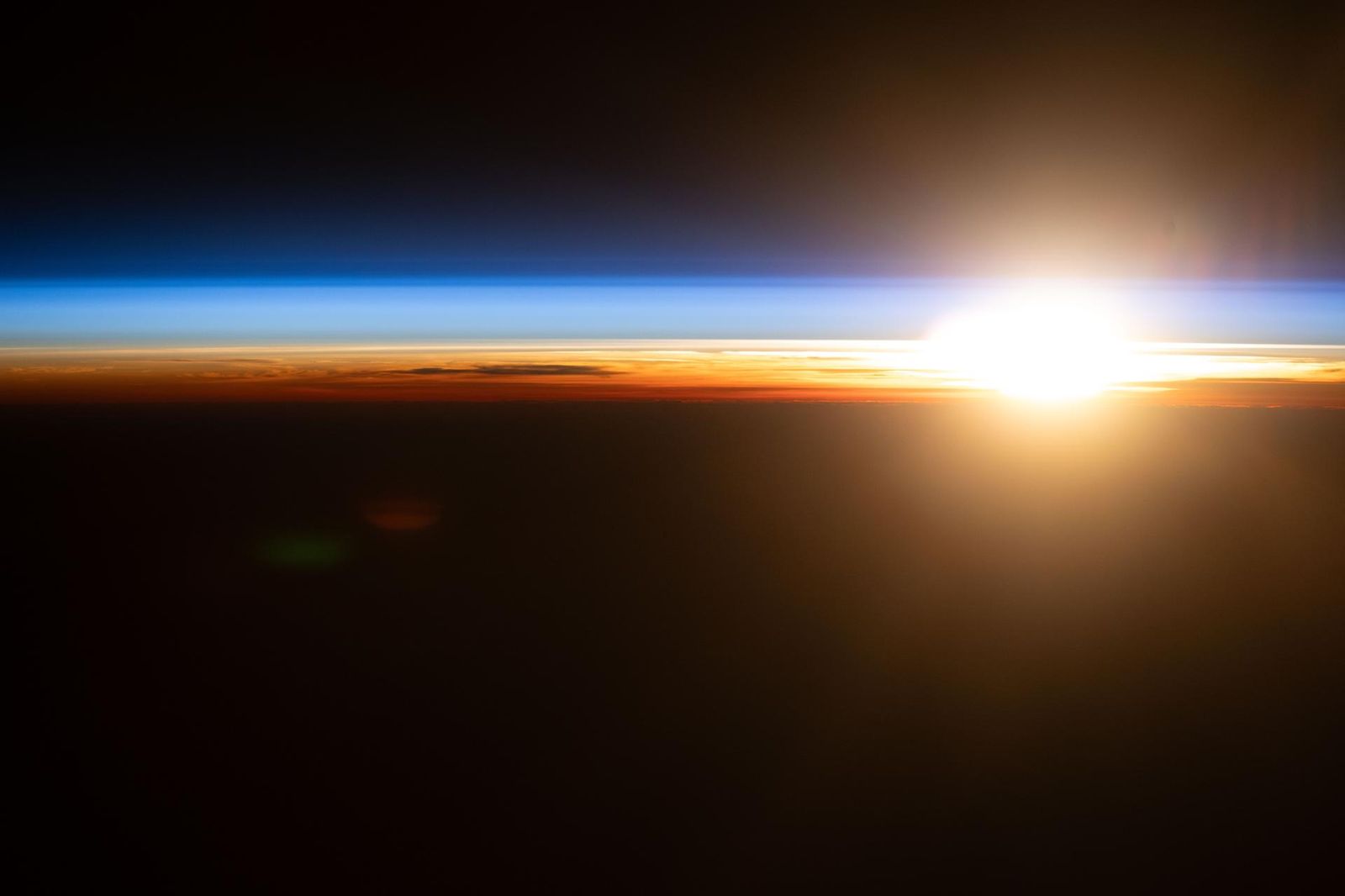An orbital sunrise above the Pacific Ocean illuminates Earth's atmosphere, revealing cloud tops and orange and blue hues outlining the planet's horizon. The International Space Station was orbiting 263 miles above the Hawaiian island chain at approximately 4:09 a.m. local time when this photograph was taken.