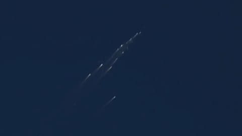 view of a satellite breaking apart, showing a dozen or so bright streaks in a blue sky