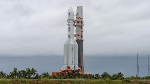 A white spacecraft standing. There are trees and grass around the bottom of it.