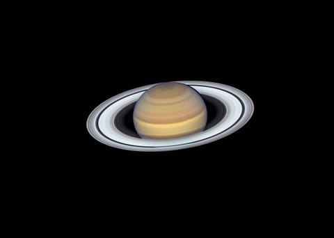 Colorful stripes in various shades of yellow, orange, and brown cover the planet. Saturn is tilted toward the viewer, allowing the Sun to illuminate the top of its rings, which appear bright white.