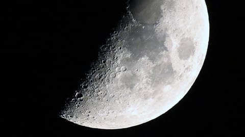 A photo of the moon with its right side lit around the first quarter phase in a black sky.