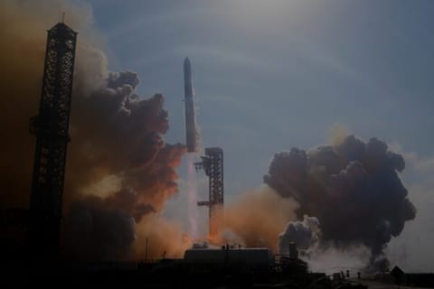 A rocket is launched from a base, large clouds are surrounding it