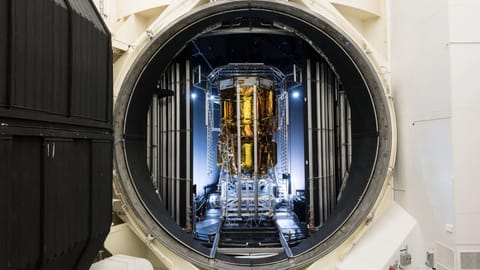 a gold-foiled spacecraft stands in a chamber with an open hatch