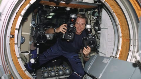 a man floats in zero gravity holding a camera in each hand