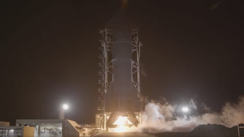 A tall finned black rocket fires an engine on a test stand in the black of night.