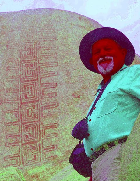 A man stands in front of a rock with art on it, the colors are intense and exaggerated revealing an intricate design in the rock's surface.