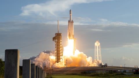 a large white rocket launches from a seaside pad