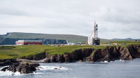 a rocket stands upright on a launch pad on a rocky outcrop beside the sea