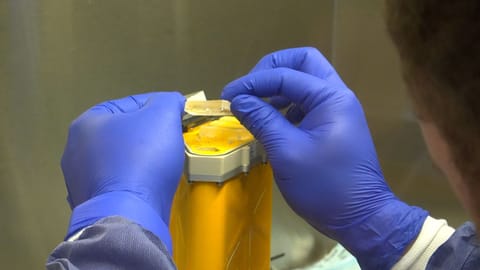 A person wearing blue gloves holds a small cylindrical organ chip.