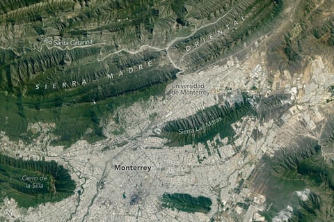 The light-colored urban development of Monterrey, Mexico, fills most of the top half of the photo, and green parallel mountain ridges arc across the bottom of the frame.