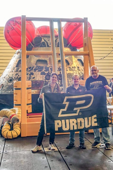 Purdue alums Emily Spreen, Jason Endsley and Rob Lantz hold up a Purdue flag in front of the Orion capsule after it returned from its journey to the moon