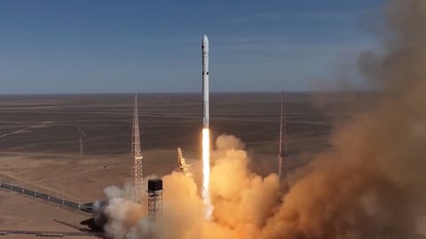 a white rocket launches into a blue sky from a desert site