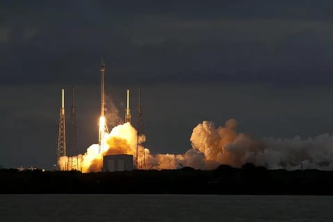 A SpaceX Falcon Heavy rocket on its launch pad at dawn, three booster cores visible, Kennedy Space Center facilities and a clear sky in the background.