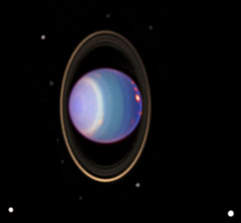 Uranus has purple, yellow, and bluish clouds forming ring-like circles around the planet. Surrounding Uranus is a ring. The whitish dots of multiple moons are visible.