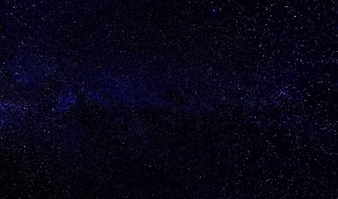 A wide-field view of distant galaxies and star clusters photographed through a telescope, showing the vast cosmic landscape that Roman will survey, with billions of stars and nebulae scattered across the frame.