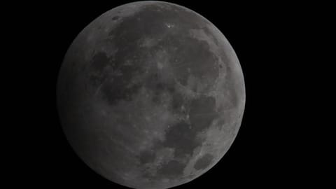 A photograph showing the penumbral stage of a lunar eclipse as the lunar disk shines in a black night's sky.