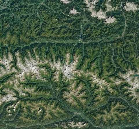 Ice in a broad Alpine basin connects with a short, narrow stretch of glacial ice in the valley below through one small icefall. Lakes fill much of the valley beyond the glacier’s terminus.