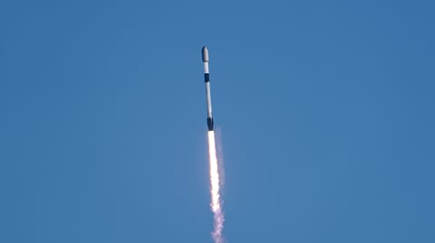 a black-and-white spacex falcon 9 rocket launches into a blue sky.