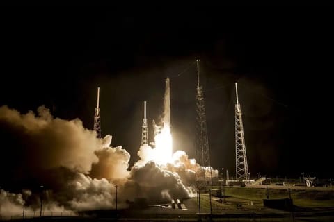 wide shot of an empty coastal launch pad at dawn, flame-retardant equipment on the pad and a gantry beside the rocket, low cloud on the horizon