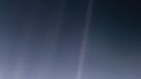A hazy blueish image has one beam of light in the center-right. There's a tiny blue dot in the beam.