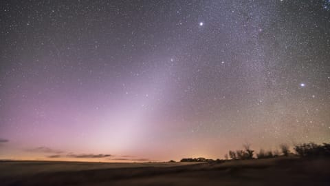 zodiacal light appears as a diffuse hazy pyramid of light spreading out across the night sky.