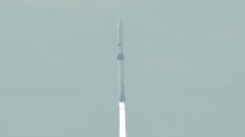 closeup of a white rocket rising into a hazy sky