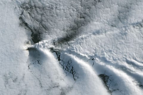 A series of V-shaped wave clouds appears over an ocean filled with pieces of sea ice.