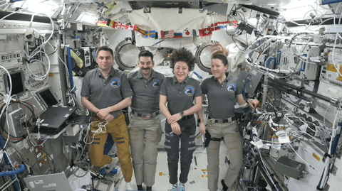 four people float in a space station module.