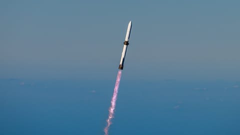 a white rocket climbs into a clear blue sky