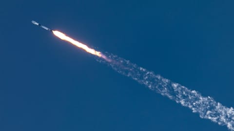 long-distance photo of a black and white rocket rising diagonally through a blue sky