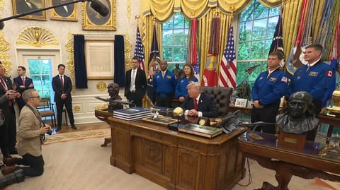 four people in blue flights stand behind a man in a suit sitting at a fancy desk